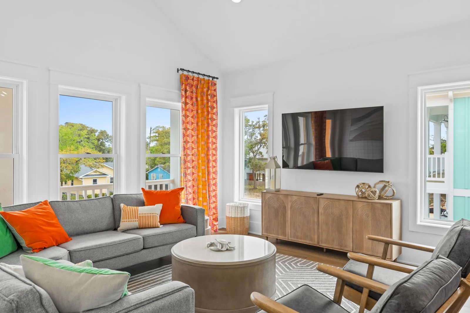 Coastal living room with gray furniture, orange accents, and natural light