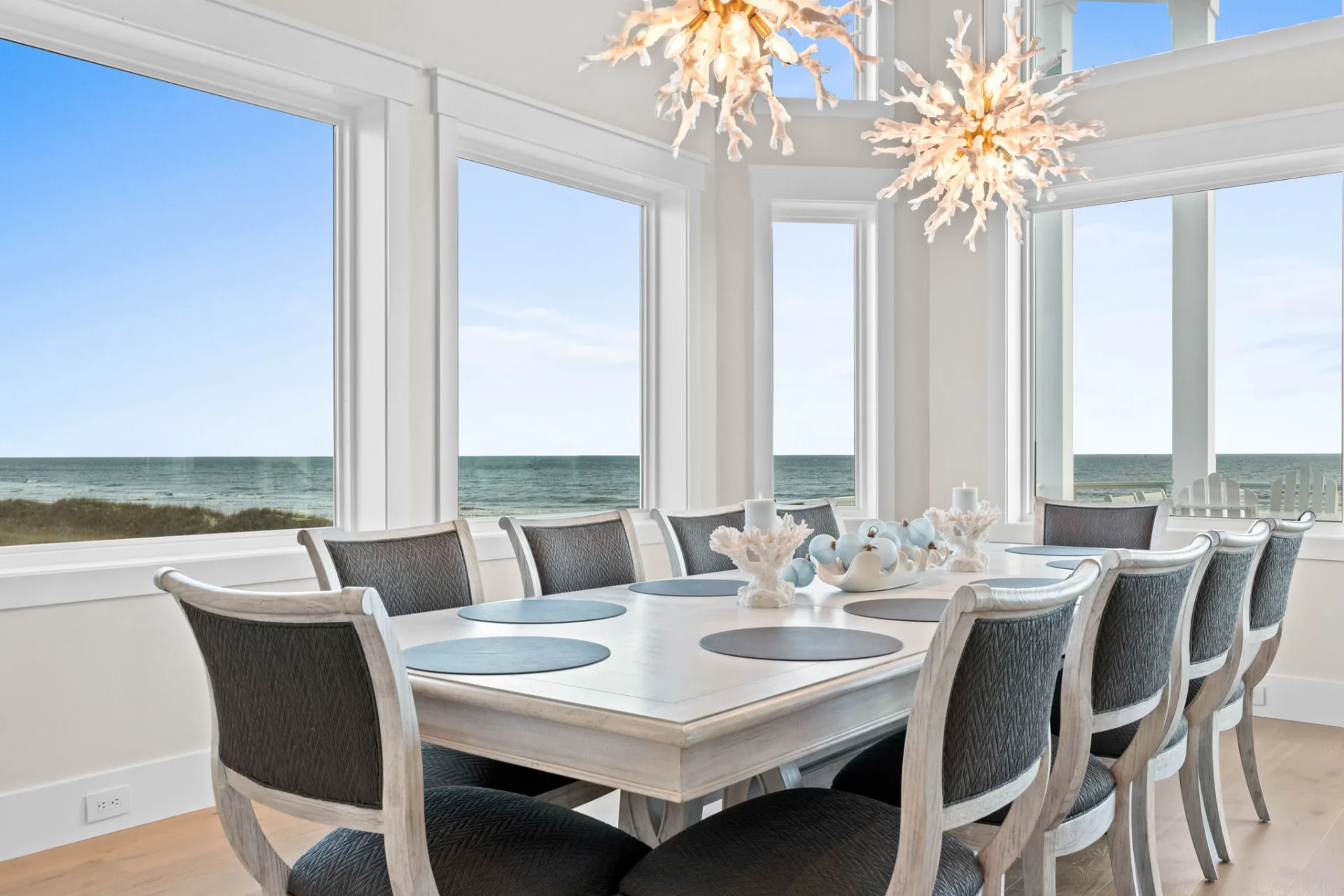 Oceanfront dining room with whitewashed table, sculptural chandeliers and windows overlooking the dunes and Atlantic Ocean
